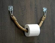 a roll of toilet paper hanging from a rope on a wooden wall with two metal hooks