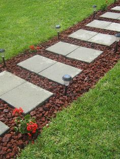 a walkway made out of stones and gravel with red flowers in the grass next to it