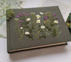 a book with flowers embroidered on it sitting on top of some papers and other items