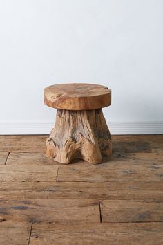 a wooden stool sitting on top of a hard wood floor next to a white wall