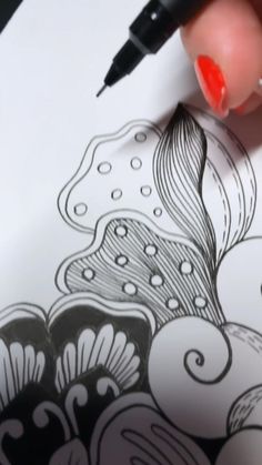 a woman's hand is holding a pen and drawing on paper with an artistic design