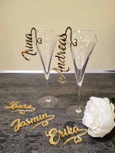 three wine glasses sitting on top of a table next to a white flower and some gold lettering