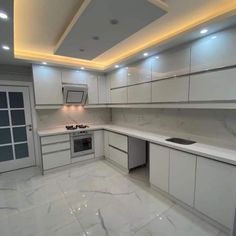 an empty kitchen with white cabinets and marble counter tops, lights above the stove top