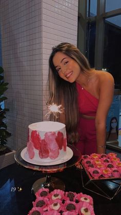 a woman standing in front of a cake with pink frosting and sprinkles