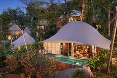 an outdoor pool surrounded by trees and white tents at night with lights on the roof