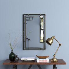 a table with a mirror, lamp and vase on it next to a bookshelf