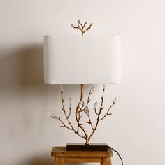 a table lamp sitting on top of a wooden stool next to a white wall with branches