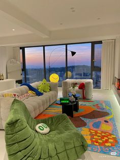 a living room filled with lots of furniture next to large windows and a colorful rug on the floor