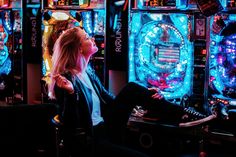 a woman sitting in front of slot machines with neon lights on the walls behind her