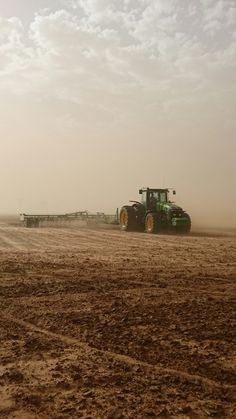 a tractor is driving in the middle of a dirt field with two other tractors behind it