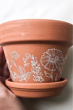 a hand holding a clay pot with flowers painted on it