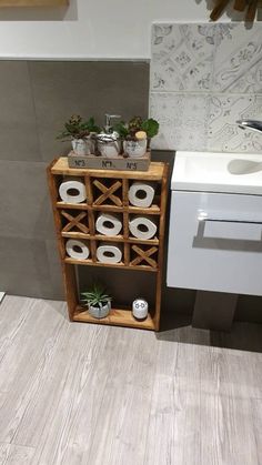 a bathroom with a sink, toilet paper holder and wooden shelf filled with rolls of toilet paper