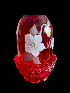 a red glass vase with white flowers on the top and bottom, against a black background