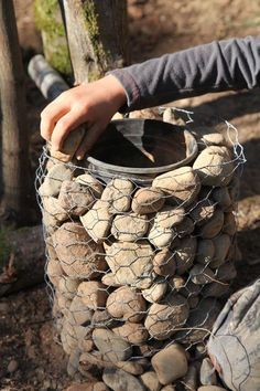 a person is holding a bucket full of rocks and mesh netting over it's sides