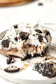 a white plate topped with a piece of cake covered in ice cream and oreo cookies