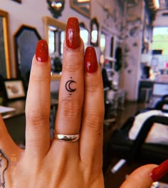 a woman's hand with a small crescent tattoo on the middle finger, and a red manicure