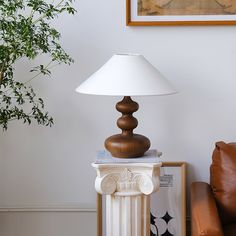 a lamp sitting on top of a white table next to a brown leather chair and potted plant