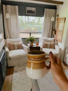 a person holding a coffee mug in front of a living room with white couches