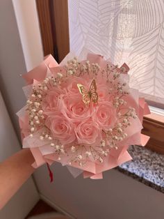 a bouquet of pink roses with a butterfly on top is held by someone's hand