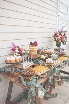 a table topped with cakes and desserts on top of a wooden table covered in greenery