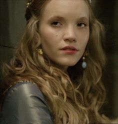 a woman with long blonde hair wearing a tiara and blue earrings in a scene from the tv game of thrones