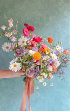 a person holding a bouquet of flowers with pink ribbon tied around the top and bottom