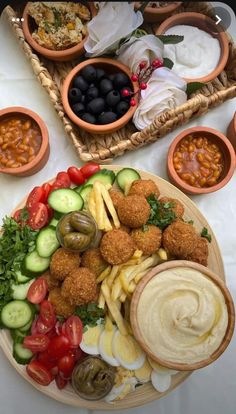 an assortment of food is displayed on a platter with bowls of beans, tomatoes and cucumbers