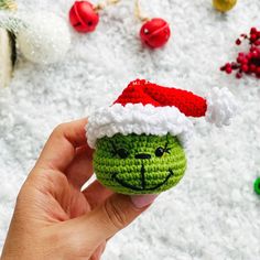 a hand holding a crocheted grin face ornament in front of christmas ornaments