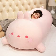 a woman laying in bed with a large pink stuffed animal on it's side