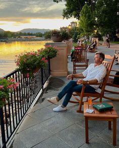 a man sitting on a wooden chair next to a lake