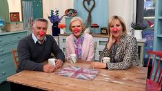 three people sitting at a table with clown noses on their faces