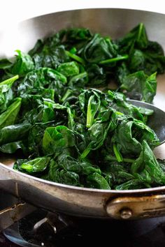 spinach leaves are being cooked in a pan on the stove top with a spoon