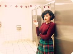 a woman in a red shirt and green plaid skirt standing next to a metal wall