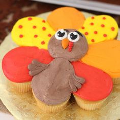 a cupcake decorated like a turkey sitting on top of a plate with frosting