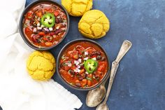 three bowls of chili and cauliflower soup with spoons next to them on a blue surface