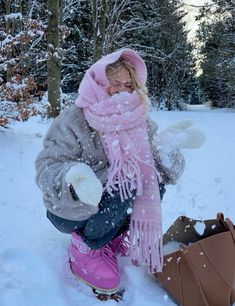 a woman kneeling down in the snow next to a teddy bear wearing a pink scarf