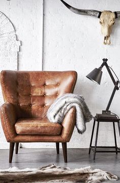 a brown leather chair sitting in front of a white brick wall next to a lamp