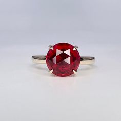 a ring with a large red stone on it's side, sitting on a white surface