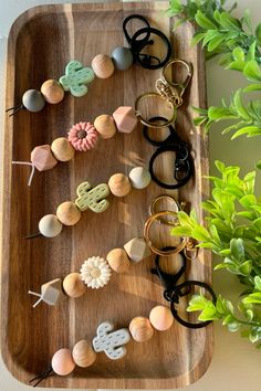 a wooden tray topped with lots of different types of buttons and rings next to a potted plant