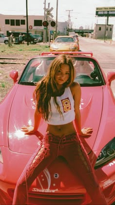 a woman standing in front of a pink sports car with her hands on her hips