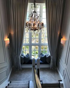 a chandelier hanging from the ceiling in front of a window with two couches