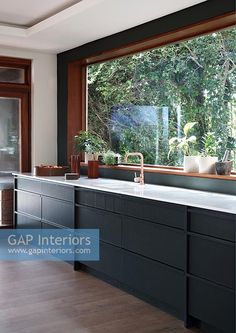 a kitchen with black cabinets and white counter tops next to a large window that looks out onto the woods