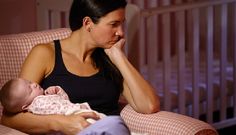 a woman sitting in a chair holding a baby and looking at the camera with her hand on her face