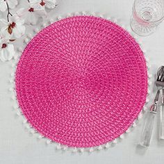 a pink placemat with white pom - poms sits next to a glass and silverware