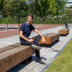 a man sitting on top of a wooden bench next to a brick walkway in a park