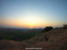 the sun is setting on top of a hill with trees in the foreground and hills in the distance