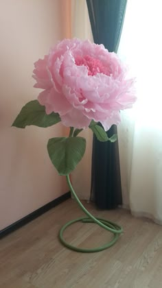 a large pink flower sitting on top of a wooden floor next to a green hose