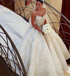 a woman in a wedding dress is walking down the stairs wearing a tiara and holding a bouquet