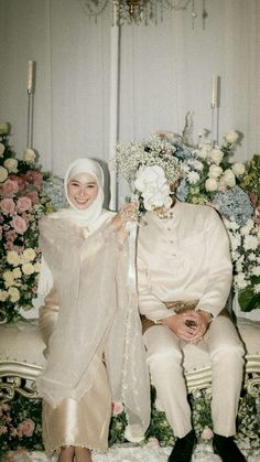 a man and woman sitting next to each other in front of flower covered wall with candles