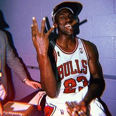 a basketball player sitting in the locker with his hand up and two other people standing behind him